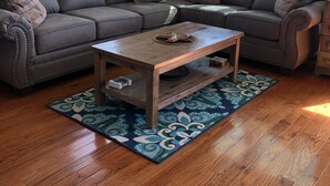 A living room with a sectional sofa, a wooden coffee table, and a patterned rug. - 10% off weeklong  stays booked now. Clean & charming oceanfront  home with view (Oak Island)