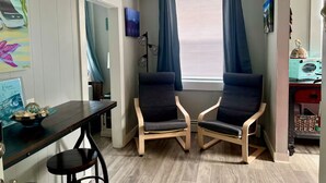 A corner room with two chairs, a table, a window with curtains, and artwork on the walls. - Marathon Historic Apartments-heart of Downtown - Charming 1 bedroom (Seward)