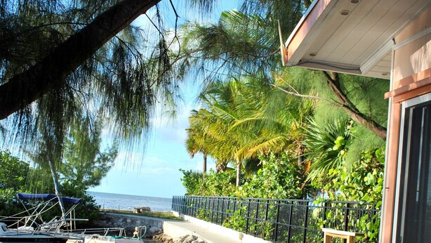 A wooden dock leading to a marina with boats, a stone wall, and a building with a glass door. - Waterfront Luxury Living Inside & Out, Gulf View, On the Water!! (Marathon)