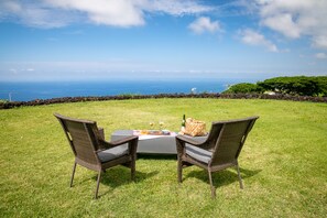 A grassy outdoor seating area with two wicker chairs and a table, overlooking a scenic ocean view. - Delightful Artful Bungalow on Historic Estate Property. Choice Holualoa!   (Holualoa)