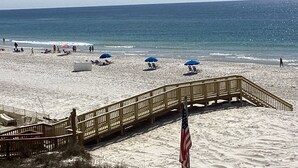 Une plage avec une promenade en bois menant à l’eau, plusieurs parasols de plage et un drapeau.