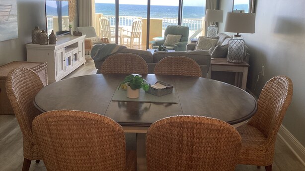 Un coin repas avec des chaises en osier, une table ronde et une vue sur l’océan grâce à de grandes fenêtres.
