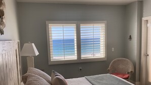 Une chambre à coucher avec un lit, une chaise, une lampe et une fenêtre donnant sur l’océan.