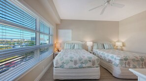 Un dormitorio con dos camas, ventilador de techo y ventana con persianas.