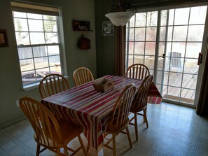 A dining area with a table set for six, wooden chairs, a striped tablecloth, and a view of the backyard through large windows. - Riverhouse Retreat on East Fork of the Bitterroot - Stunning Views & Tranquility (Conner)