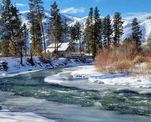 A house by a river with snow-covered mountains in the background. - Riverhouse Retreat on East Fork of the Bitterroot - Stunning Views & Tranquility (Conner)
