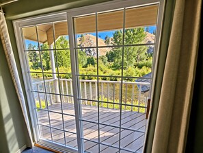 A view through a window with a metal grid, overlooking a wooden deck and a natural landscape with trees and hills. - Riverhouse Retreat on East Fork of the Bitterroot - Stunning Views & Tranquility (Conner)