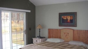 A bedroom with a bed, a nightstand, a lamp, a painting, and a sliding glass door leading to an outdoor area. - Riverhouse Retreat on East Fork of the Bitterroot - Stunning Views & Tranquility (Conner)