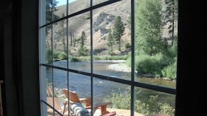 A view of a river through a window with outdoor seating. - Riverhouse Retreat on East Fork of the Bitterroot - Stunning Views & Tranquility (Conner)