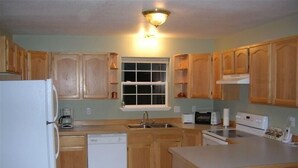 A kitchen with wooden cabinets, a refrigerator, a dishwasher, a sink, a window, and a countertop. - Riverhouse Retreat on East Fork of the Bitterroot - Stunning Views & Tranquility (Conner)