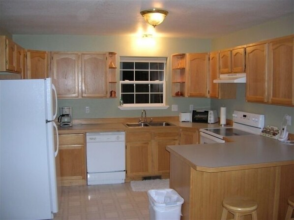 A kitchen with wooden cabinets, a refrigerator, a dishwasher, a sink, a window, and a countertop. - Riverhouse Retreat on East Fork of the Bitterroot - Stunning Views & Tranquility (Conner)