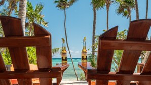 Two wooden chairs with a view of the beach and palm trees.