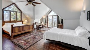A bedroom with a sloped ceiling, a wooden bed, a chair, a TV, and a view of trees through large windows. - Ski In/Out-Sleeps 18, 9,000 Sq Ft-Hot Tub-Pool Table-Mtn Views-Theatre Rm (Breckenridge)