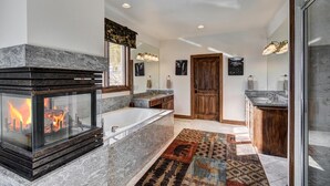 A modern bathroom with a fireplace, a large bathtub, and a walk-in shower. - Ski In/Out-Sleeps 18, 9,000 Sq Ft-Hot Tub-Pool Table-Mtn Views-Theatre Rm (Breckenridge)