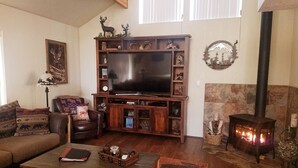 A cozy living room with a large flat-screen TV, a fireplace, and a bookshelf filled with decorative items. -  "Palms to Pines Cabin" - Your home away from home... ☆ 5/5 ☆ Star Rated (Pine)