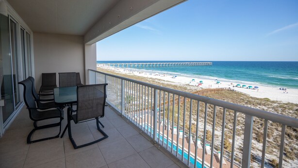 A balcony with a table and chairs overlooking a beach with a pier. - Navarre's best views from this Regency end unit (Navarre Beach)