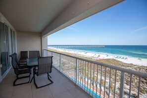 Ein Balkon mit Tisch und Stühlen mit Blick auf einen Strand und einen Steg.