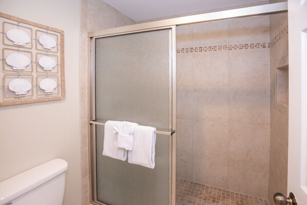 Un espace douche doté d’une porte en verre, d’un porte-serviettes avec des serviettes et d’une décoration murale en forme de coquillage.