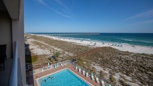 A beach view from a balcony with a pool, beach umbrellas, and a pier in the distance. - Navarre's best views from this Regency end unit (Navarre Beach)