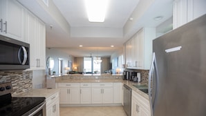 A modern kitchen with white cabinets, a stainless steel refrigerator, a microwave, and a stove. - Navarre's best views from this Regency end unit (Navarre Beach)