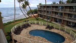 A pool with a stone border, surrounded by a white fence, overlooking a beach and ocean. - End Unit Yards from Ocean Looking East With Major Sunrises (Kapaa)