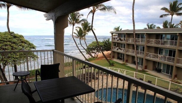 A balcony with a table and chairs overlooking a pool and a beach. - End Unit Yards from Ocean Looking East With Major Sunrises (Kapaa)