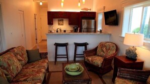 A compact living space with a kitchen area, two bar stools, a sofa, and a coffee table. - End Unit Yards from Ocean Looking East With Major Sunrises (Kapaa)