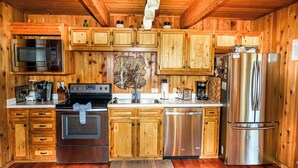 Una cocina tipo cabaña de madera con microondas, horno, refrigerador y armarios de madera.