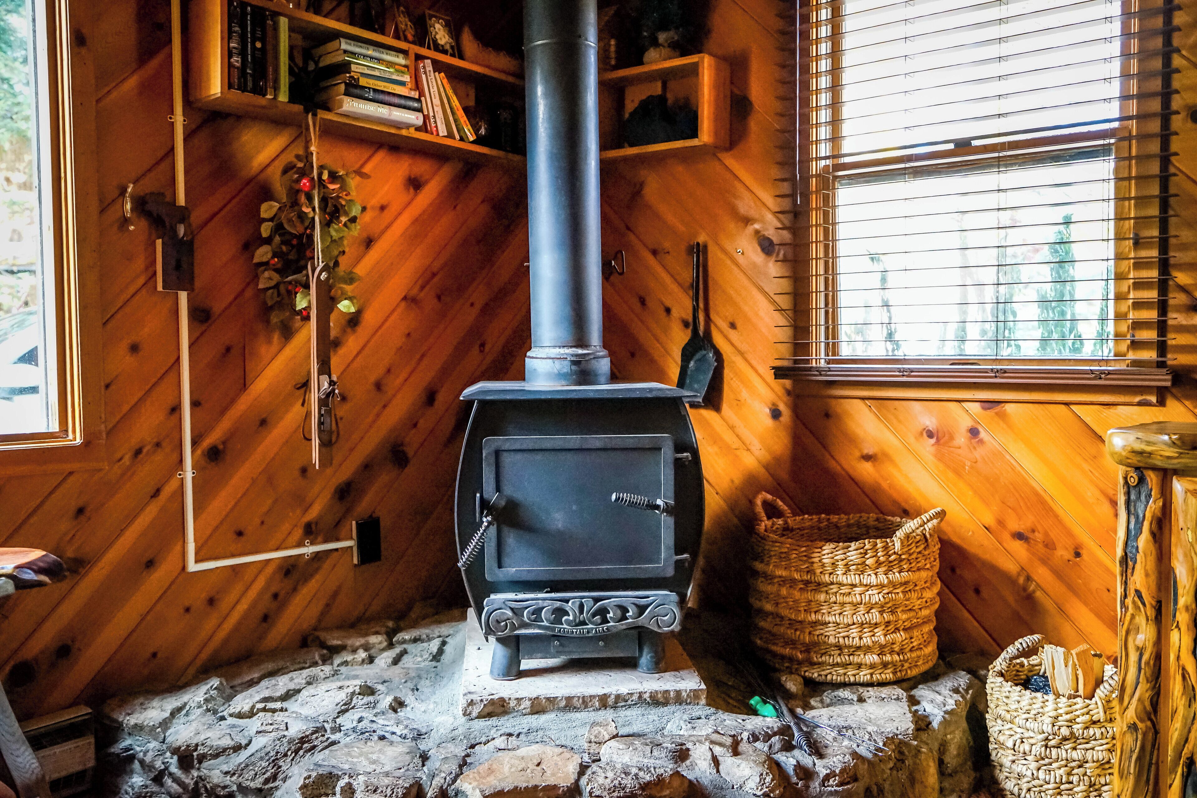 Una habitación acogedora con chimenea de leña, suelo de piedra, paredes de madera y una ventana con persianas.