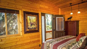 Un dormitorio tipo cabaña de madera con cama, un cuadro enmarcado de un caballo, una puerta y una ventana.