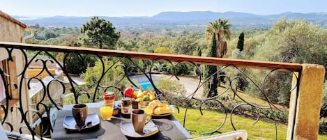Un balcon avec une table dressée pour le petit-déjeuner, offrant une vue panoramique sur un paysage magnifique, avec des arbres et des montagnes.