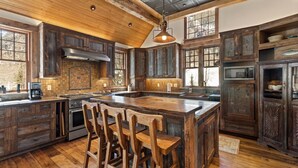 A rustic kitchen with wooden cabinets, a large island with bar stools, a stove, and a microwave. - Telluride Riverfront House with Mountain Views (Telluride)