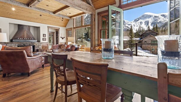 A cozy living room with a fireplace, wooden furniture, and a view of snow-capped mountains. - Telluride Riverfront House with Mountain Views (Telluride)