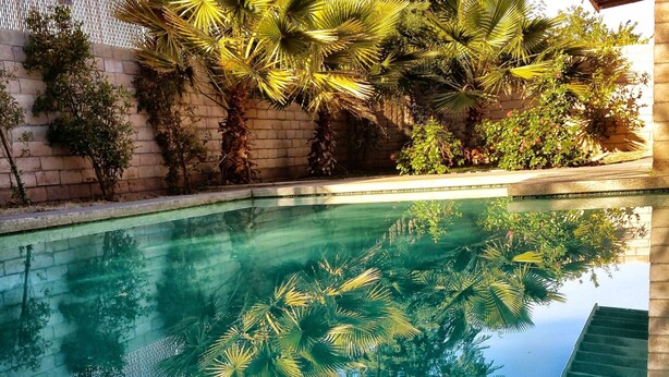 A clear swimming pool with a reflection of surrounding trees and a wooden structure. - Make Your Friends Jealous (Indio)