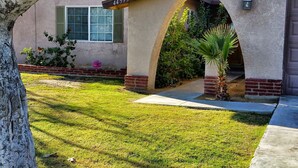 A residential property with a well-maintained lawn, a tree, and a house featuring a stucco exterior, an arched entrance, and a mailbox. - Make Your Friends Jealous (Indio)