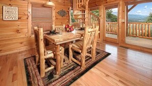 Un interior de madera con una mesa y sillas de comedor, una escalera y vistas al exterior.