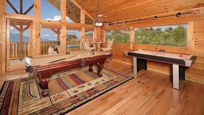Interior de madera con mesa de billar, sillas y vistas al exterior.