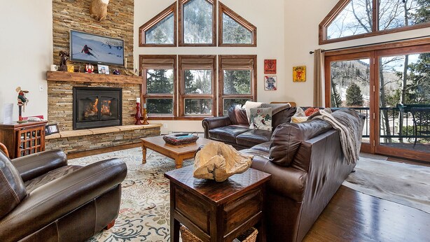 A spacious living room with a stone fireplace, leather sofas, and large windows offering views of the outdoors.