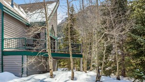 A house with a green balcony overlooking a snowy landscape and trees.