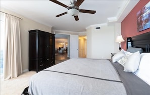 Une chambre d’hôtel avec un grand lit, un ventilateur de plafond, une armoire en bois sombre et une vue sur un couloir et une autre chambre.