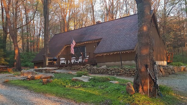 A rustic cabin with a stone foundation, a wooden deck, and an American flag. - Seven Springs Cabin - Fox Tail Chalet - Authentic, Pet Friendly Log Cabin Chalet (Champion)