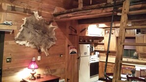 A rustic cabin interior with wooden walls, a mounted animal hide, a refrigerator, and a wooden ladder. - Seven Springs Cabin - Fox Tail Chalet - Authentic, Pet Friendly Log Cabin Chalet (Champion)