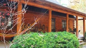 A wooden cabin with a covered porch, a fire pit, and a well-maintained garden.