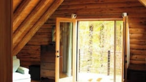 A log cabin bedroom with a bed, a desk, and a window with a view of the outdoors.