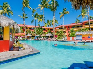 Een zwembad bij een resort met helderblauw water, palmbomen en kleurrijke gebouwen.