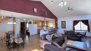 A spacious living area with a dining table, sofas, and a kitchen in the background. - The McCaskell Cabin- Nestled out in the countryside.  (Hill City)