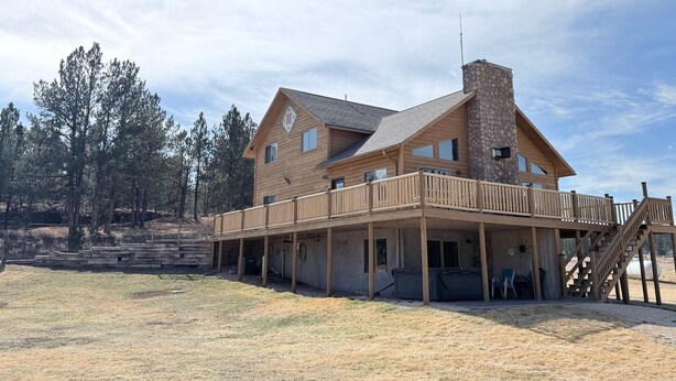 A two-story wooden cabin with a stone chimney, a covered deck, and a stone retaining wall. - The McCaskell Cabin- Nestled out in the countryside.  (Hill City)
