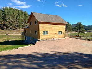 A wooden cabin with a sloped roof, a gravel driveway, and a fenced pasture with a horse. - The McCaskell Cabin- Nestled out in the countryside. (Hill City)