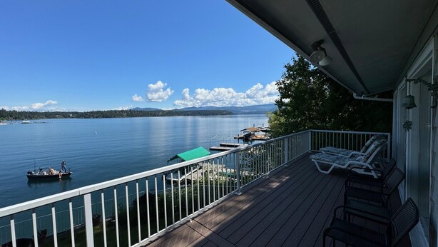Une terrasse en bois offrant une vue sur un lac, un bateau et une chaîne de montagnes lointaine.
