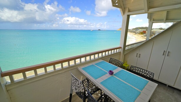 A balcony with a table and chairs, overlooking a beach and the ocean. - Grand Case beach (Grand Case)